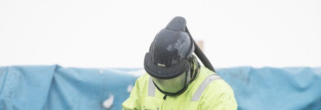 Person in a high visibility coat and full face mask looking down