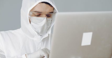 Man in coveralls and dust mask at his computer